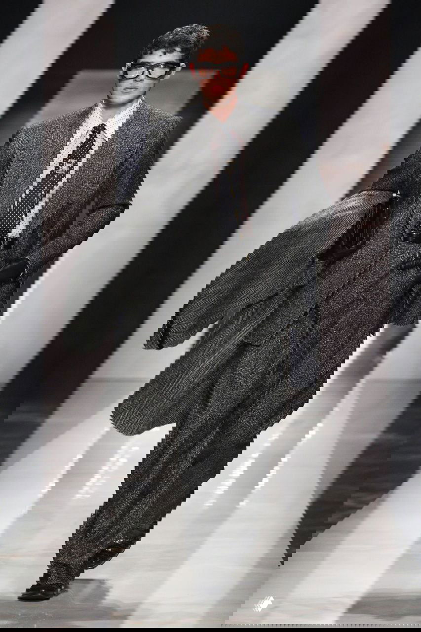 Мужской образ в строгом сером костюме, очках и перчатках на подиуме Gucci в Милане — акцент на интеллектуальный архетип осенней коллекции бренда.