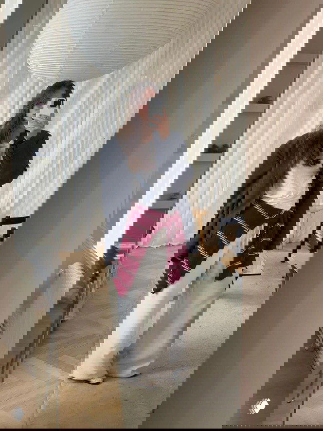 Селфи в зеркале: широкие белые брюки в сочетании с белой футболкой и тёмным оверсайз‑пиджаком, светлая комната с крупной подвесной лампой на фоне.