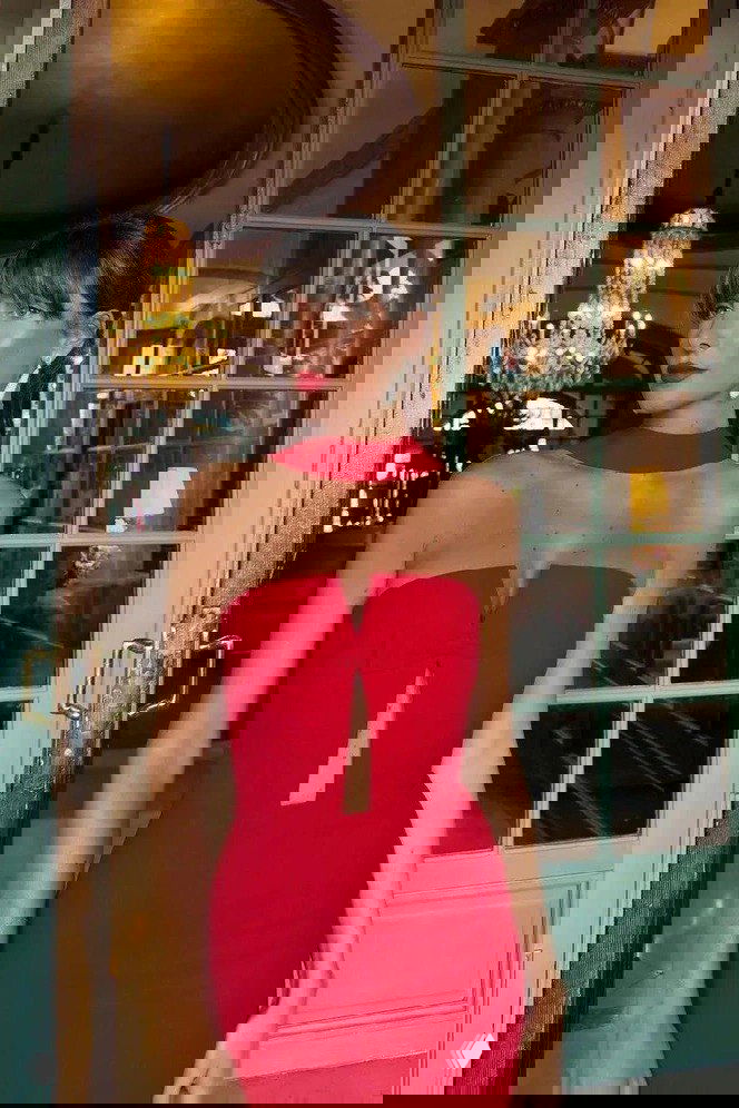 Модель в алом облегающем платье-бюстье на фоне люстры и стеклянной двери — акцент на цвет и минималистичный крой праздничного наряда