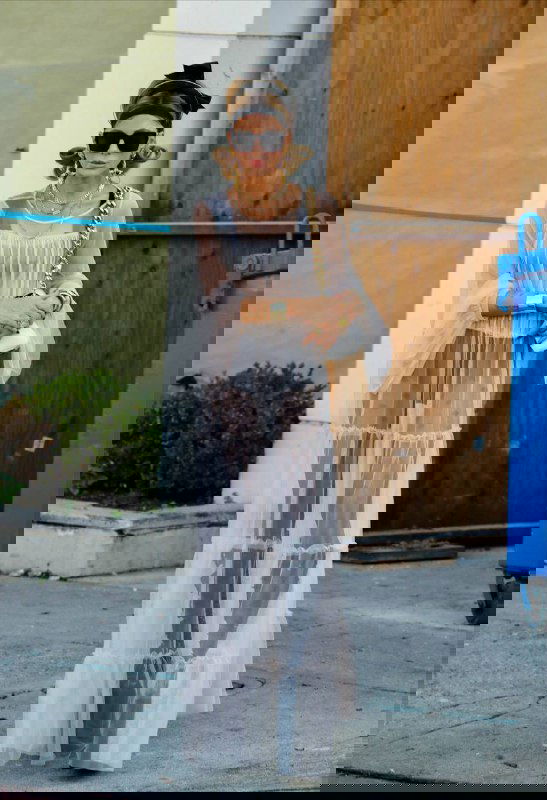 Модный образ в прозрачном лёгком платье и аксессуарах на фоне фасада здания — летящий тканевый силуэт в уличной съёмке.