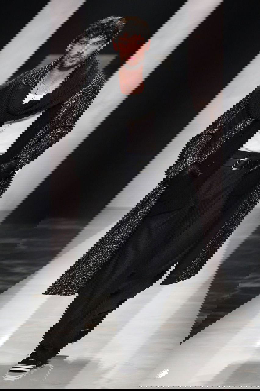 Модель в длинном пальто и шарфе поверх белой футболки и тёмных брюк на показе Gucci — свободный, но благородный мужской силуэт для осени.