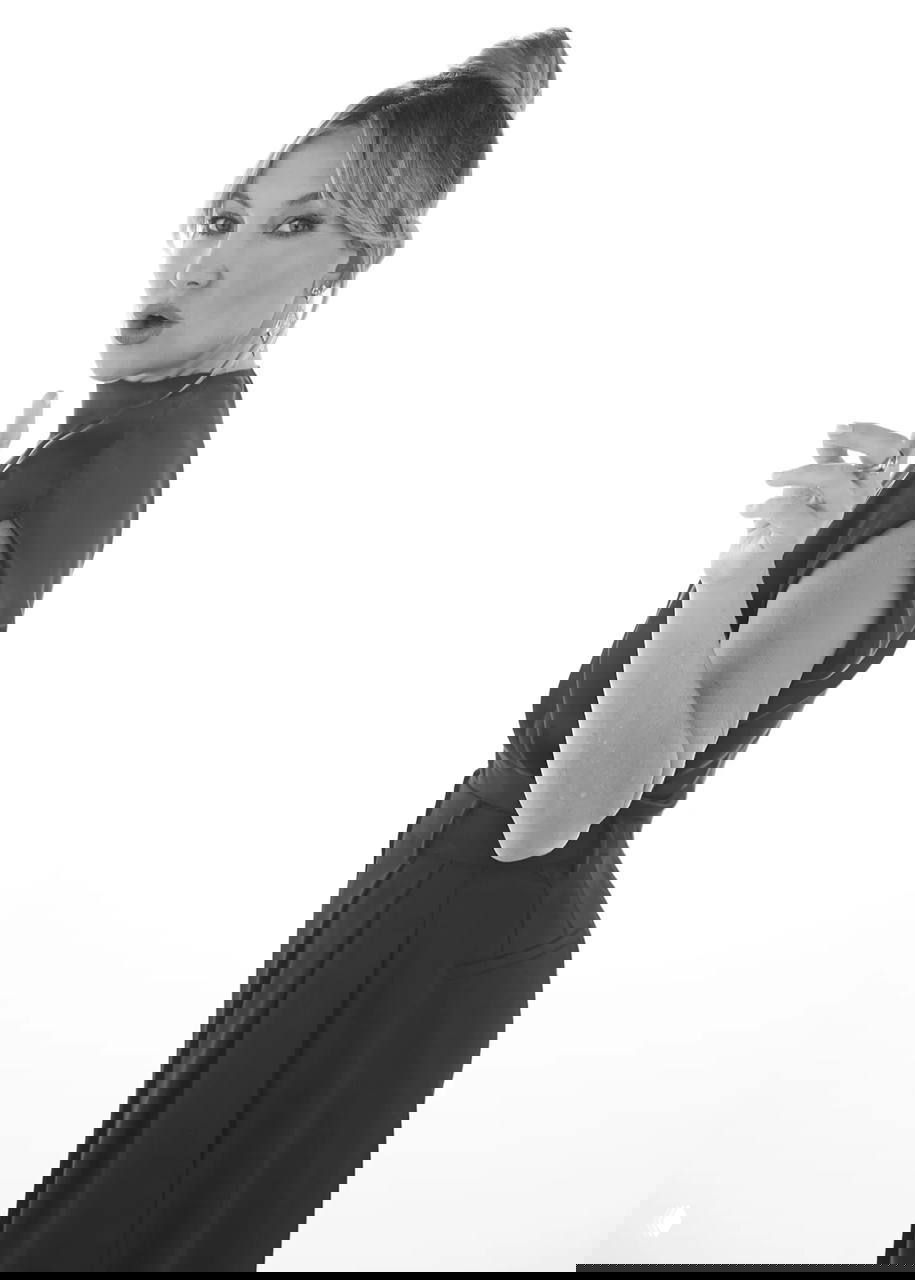 Чёрно‑белый ростовой кадр Кейт Хадсон в студии: элегантное платье, причёска и серьги, выразительный жест рукой как элемент образа.