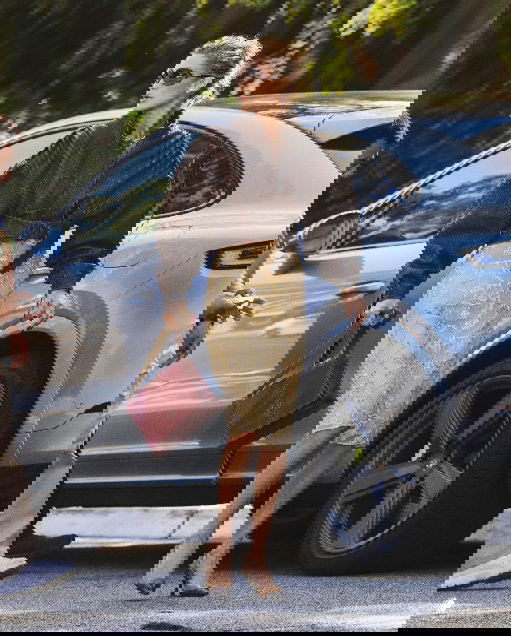 Белла Хадид в Лос‑Анджелесе: светлое вышитое винтажное платье и объёмная коричневая кожаная куртка на фоне припаркованного автомобиля.