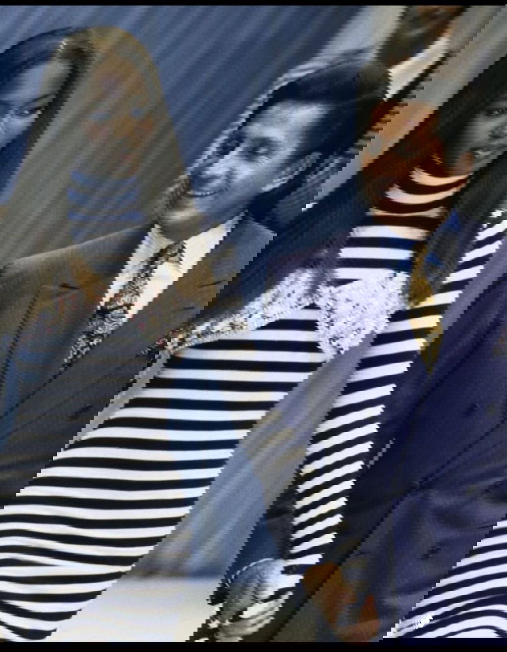 Модель в тельняшке и тёмном жакете идёт по подиуму рядом со взрослым мужчиной в пиджаке — архивный показ с эффектной динамикой.