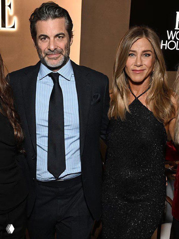 Актриса в чёрном сияющем платье позирует рядом с мужчиной в классическом костюме и светло-голубой рубашке на церемонии.