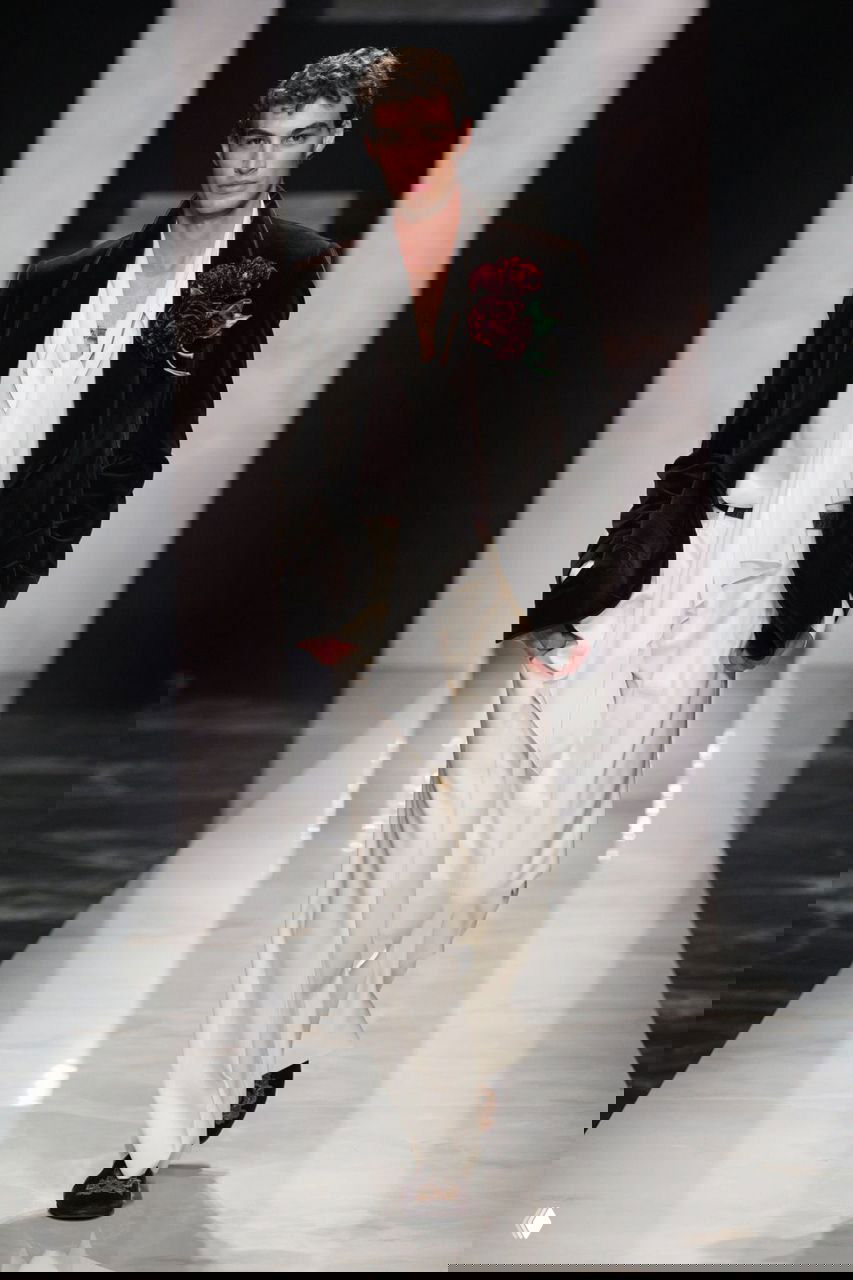 Модель в белой рубашке с драпировкой и тёмном бархатном пиджаке с цветочной брошью демонстрирует романтический архетип Gucci на миланском показе.