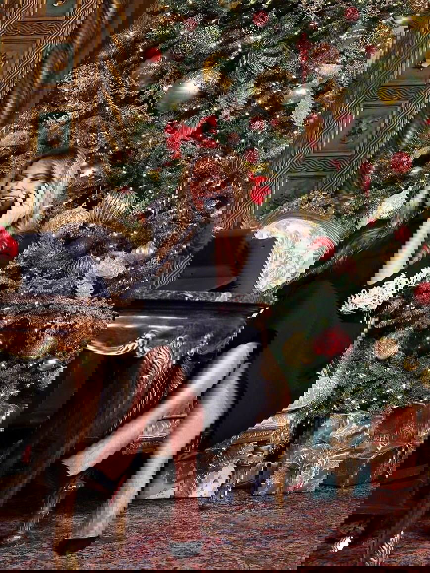 Мелания Трамп говорит по телефону, сидя в кресле у украшенной ёлки; кадр подчёркивает праздничный интерьер и аксессуары события.