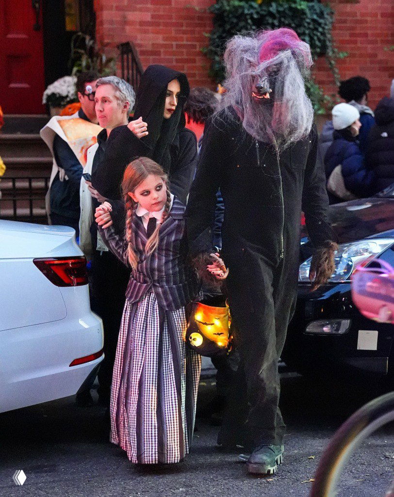 Ирина Шейк и Брэдли Купер с дочерью Леей в хэллоуинских костюмах идут по улице; у девочки светящийся фонарь.