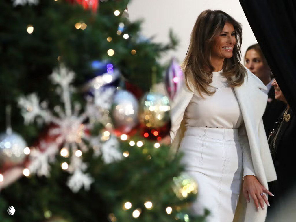 Крупный план женщины в светлом пальто возле нарядной рождественской ёлки: боке гирлянд, праздничные игрушки и теплая атмосфера.