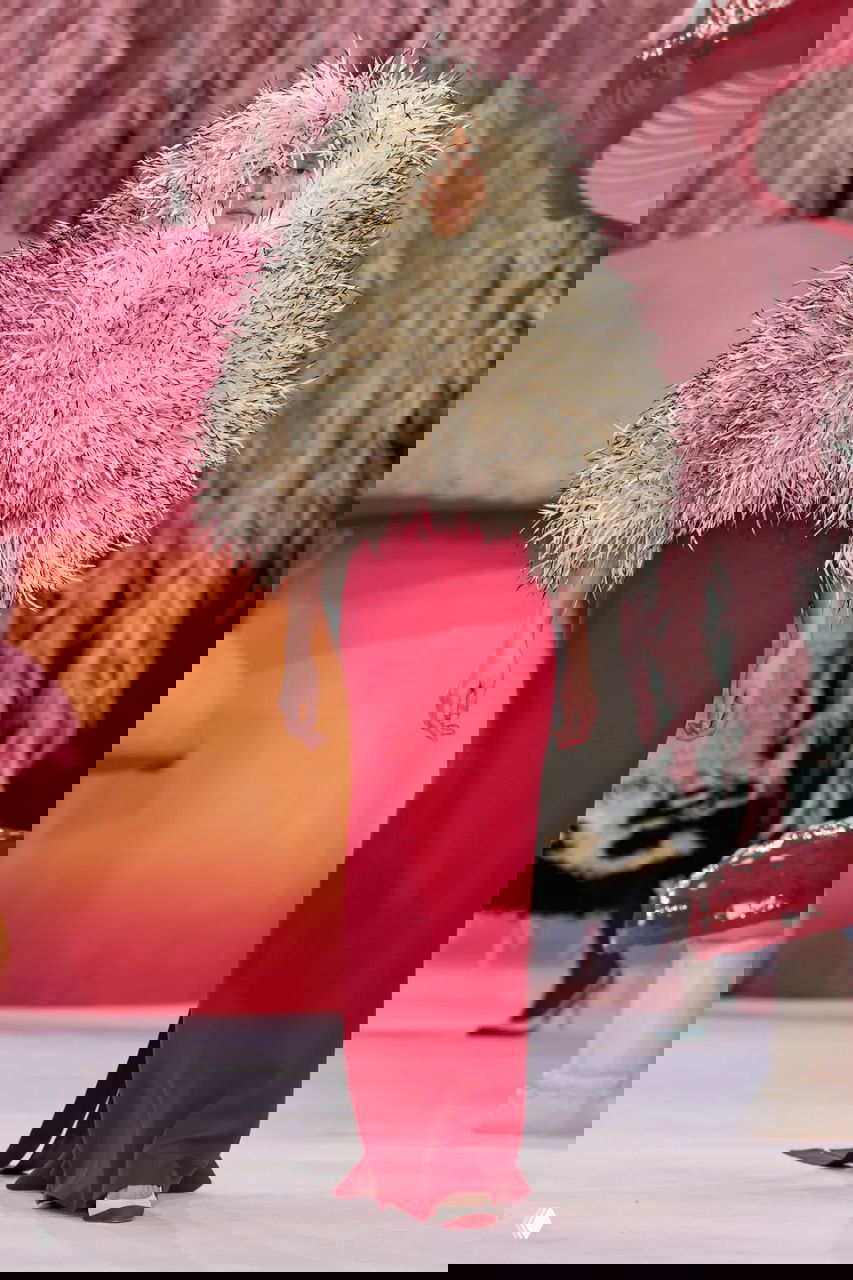 Высокая модель в красном платье с объёмным пушистым накидом идёт по подиуму Chanel — эффектный образ на фоне сказочного декора шоу.