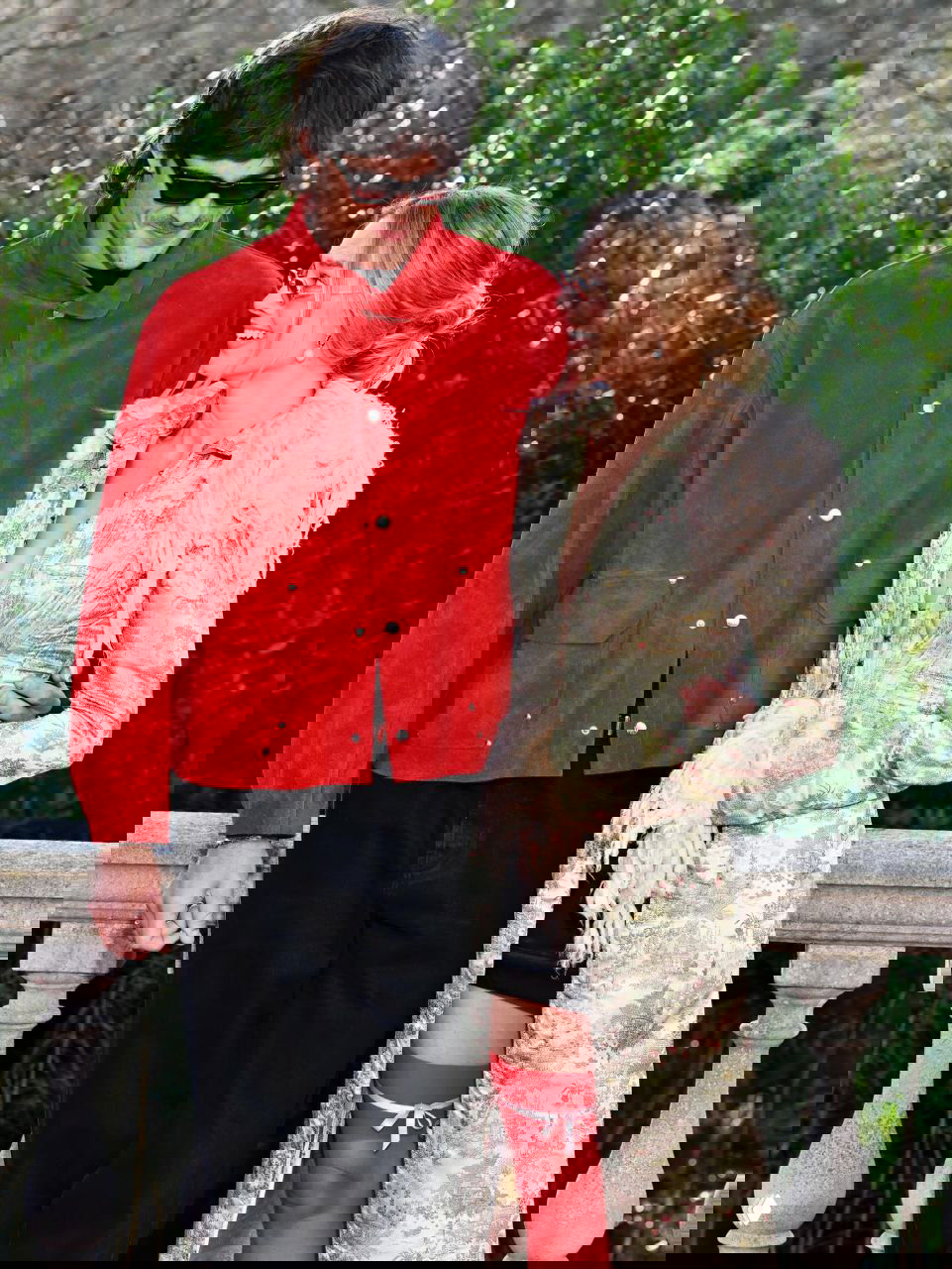 Пара на прогулке: женщина в длинном пальто с перьевыми деталями и мужчина в красной куртке, естественная сценка на свежем воздухе