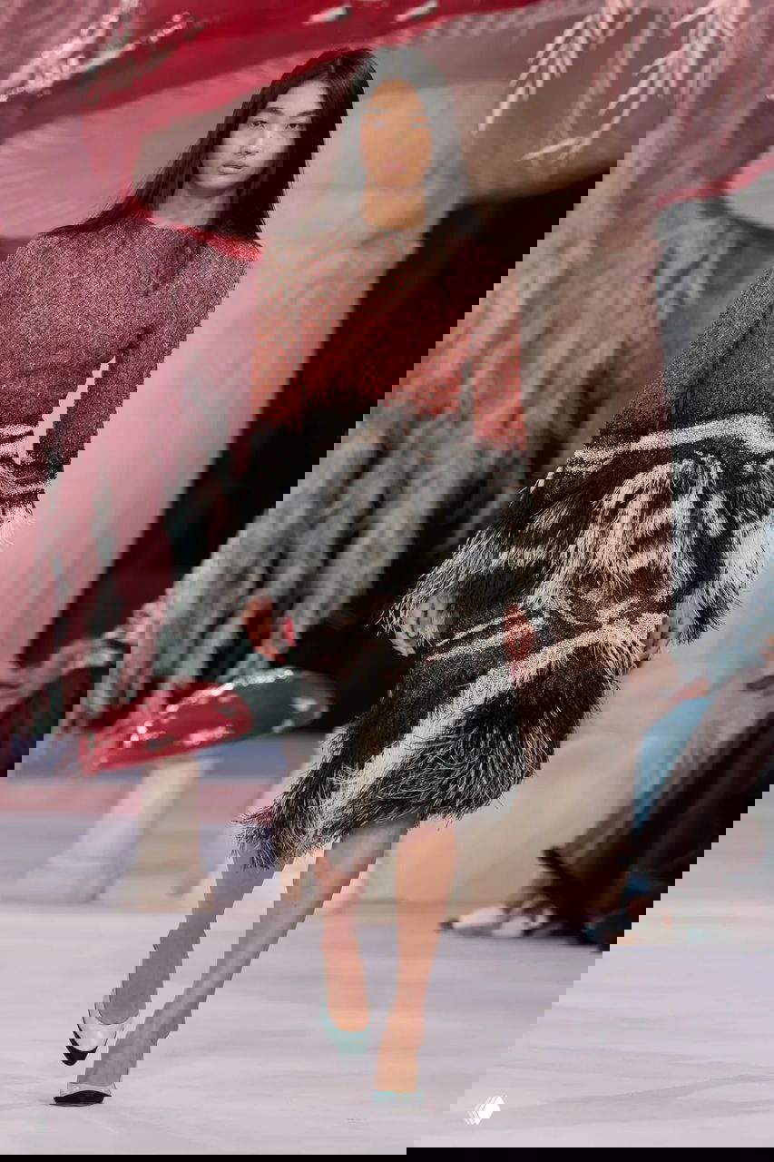 Модель в текстурированном платье с контрастной чёрно-белой низкой бахромой шагает по подиуму Chanel на фоне розово-пастельного оформления.