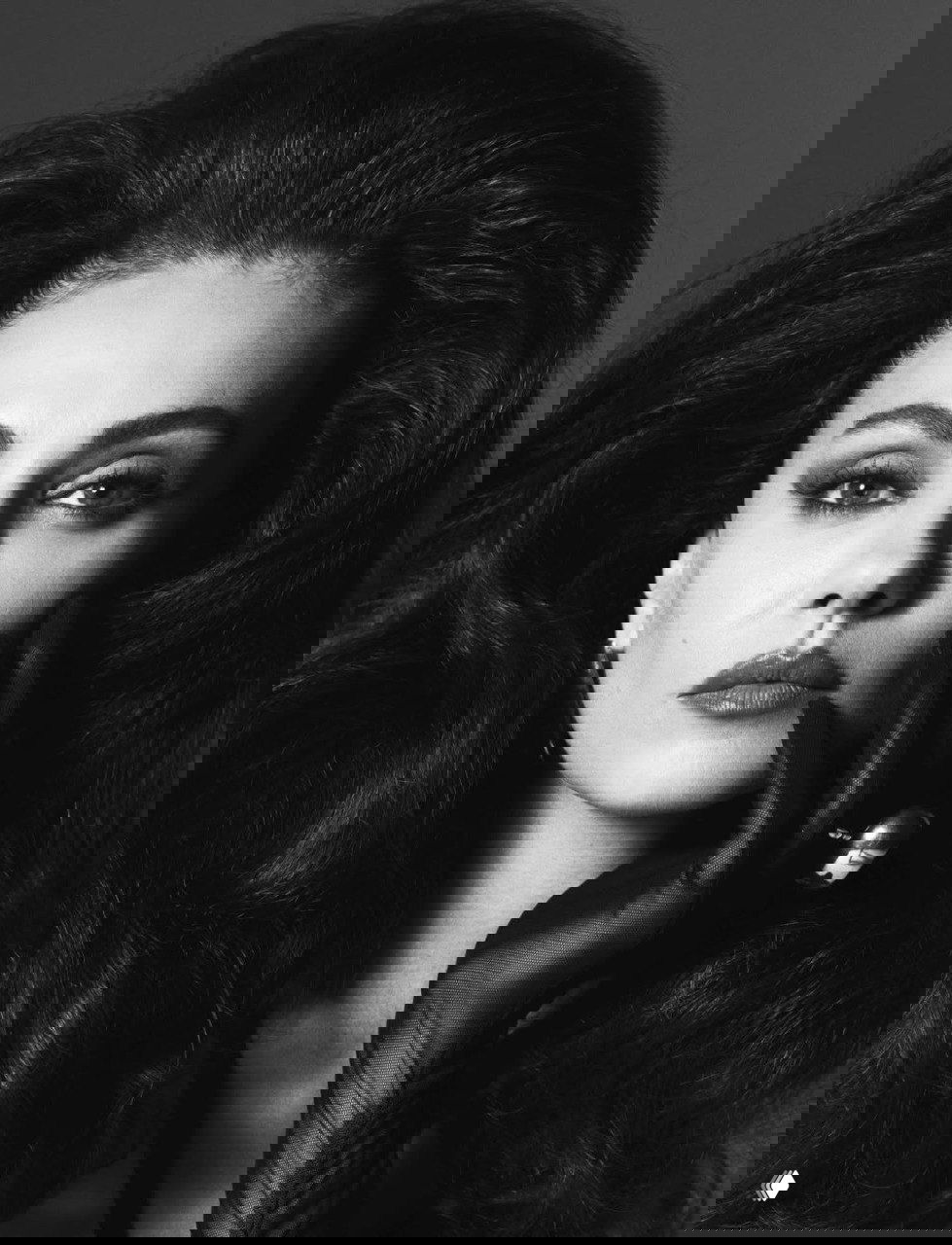 Ближний план лица с выразительными глазами, тонким макияжем и перчаткой у подбородка, гламурная черно‑белая эстетика.