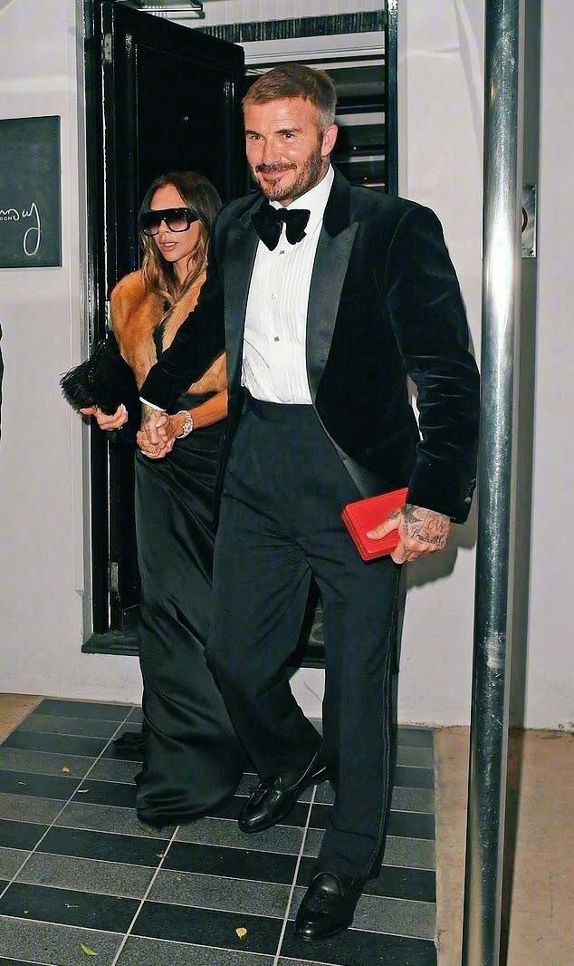 Мужчина в чёрном смокинге с красным клатчем держит руку женщины в вечернем платье, выходя на афтерпати после посвящения.