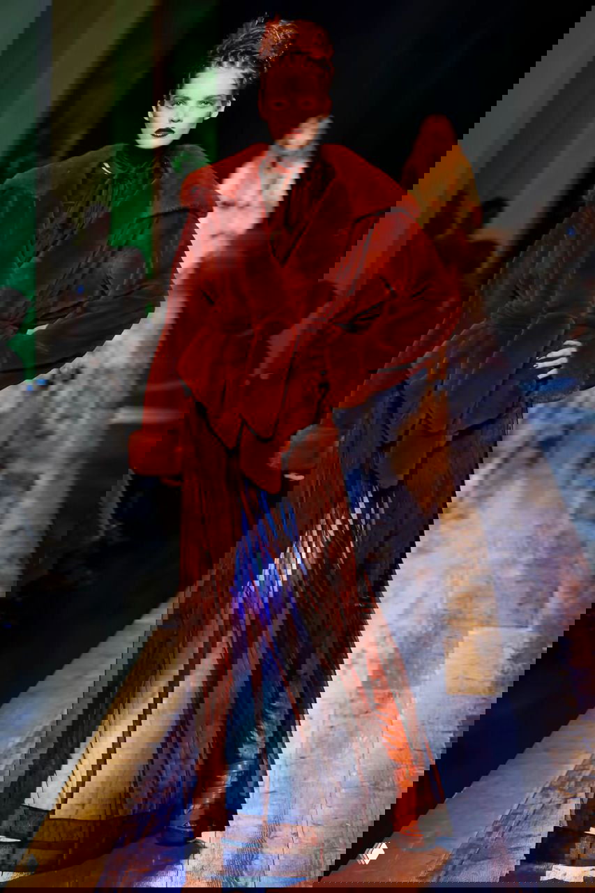 Модель в тёмно-красном бархатном пальто и прозрачной юбке на деревянной дорожке подиума — кутюрный показ 2016.