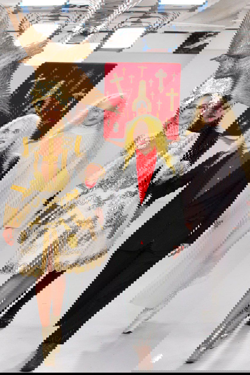 Пэм Хогг на подиуме в окружении моделей в экстравагантных костюмах: дизайнер с яркими желтыми волосами и характерным сценическим образом.