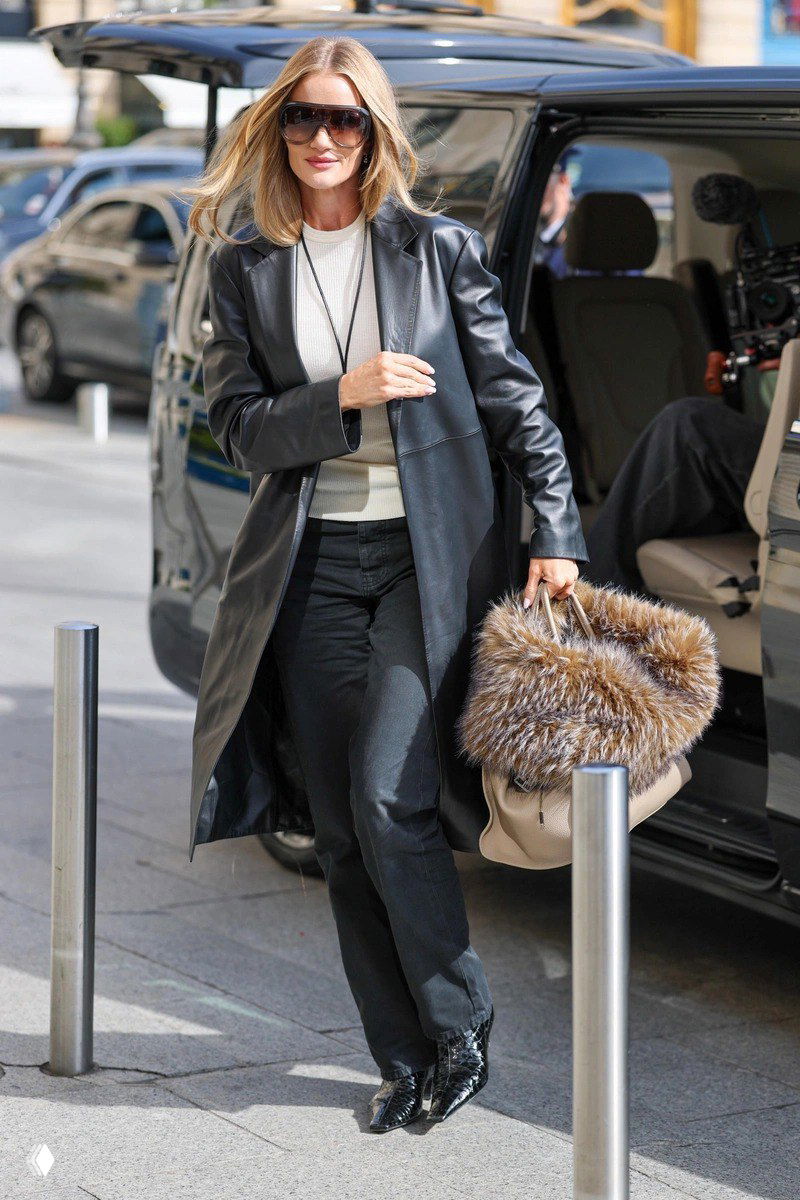 Роузи Хантингтон-Уайтли выходит из автомобиля в длинном чёрном кожаном плаще и чёрных джинсах, с объёмной меховой сумкой.