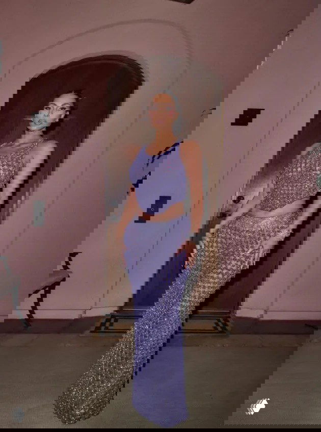 Женщина в сиреневом блестящем костюме-платье позирует у арочного дверного проёма; съёмка в помещении перед входом.