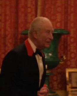 Король Карл в смокинге на премьере; фон — богато оформленный зал с красными портьерами и декоративными деталями интерьера.