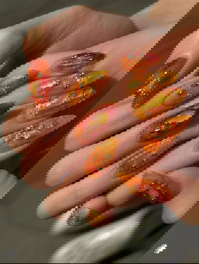 Длинные миндалевидные ногти в тёплых оранжево‑золотых тонах с объёмным гелевым дизайном и металлическими бусинами — осеннее вдохновение на фото.