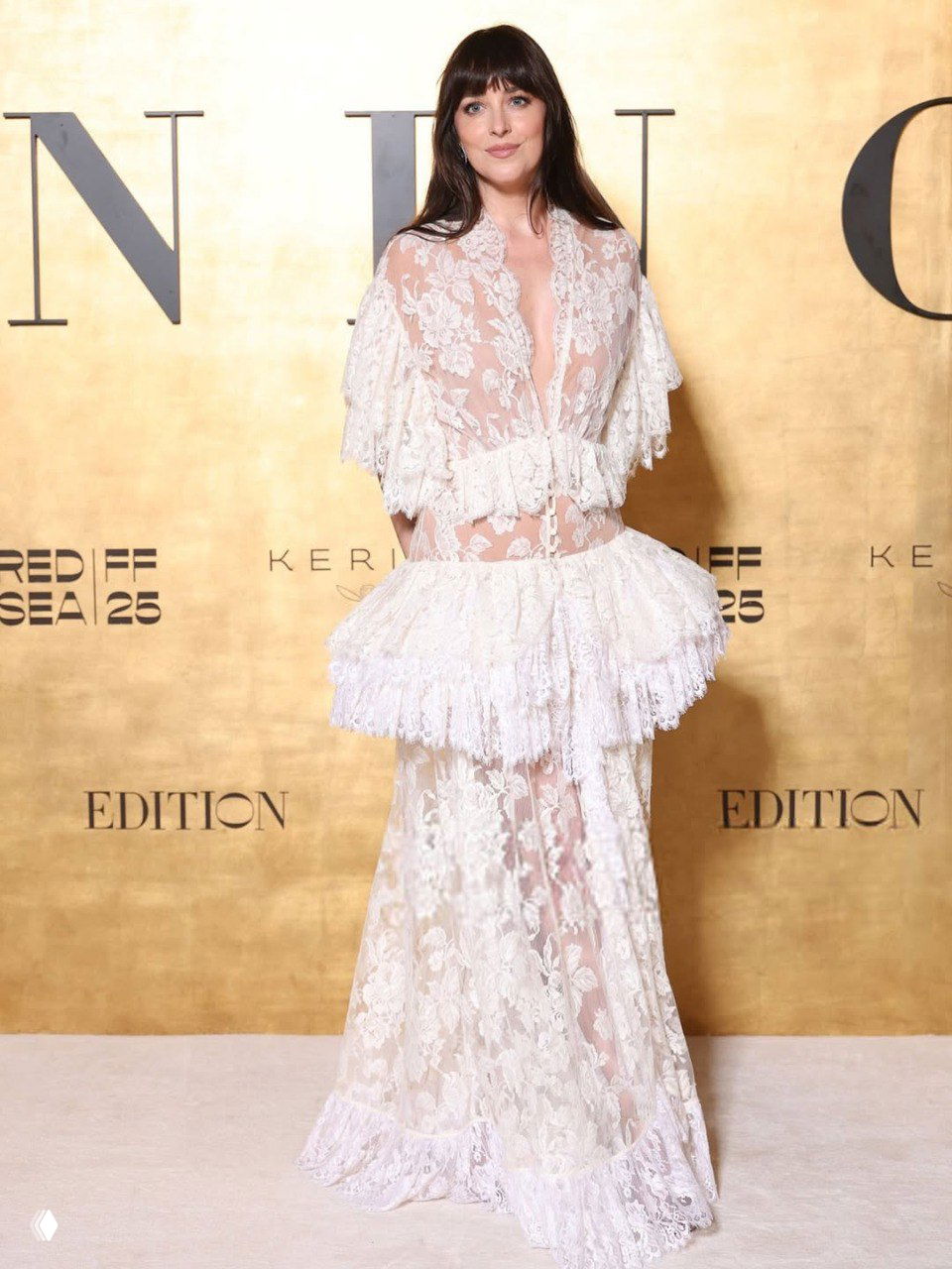 Дакота Джонсон в белом кружевном платье Chloé: полный рост, прозрачная фактура, многослойная юбка и золотой фон мероприятия.