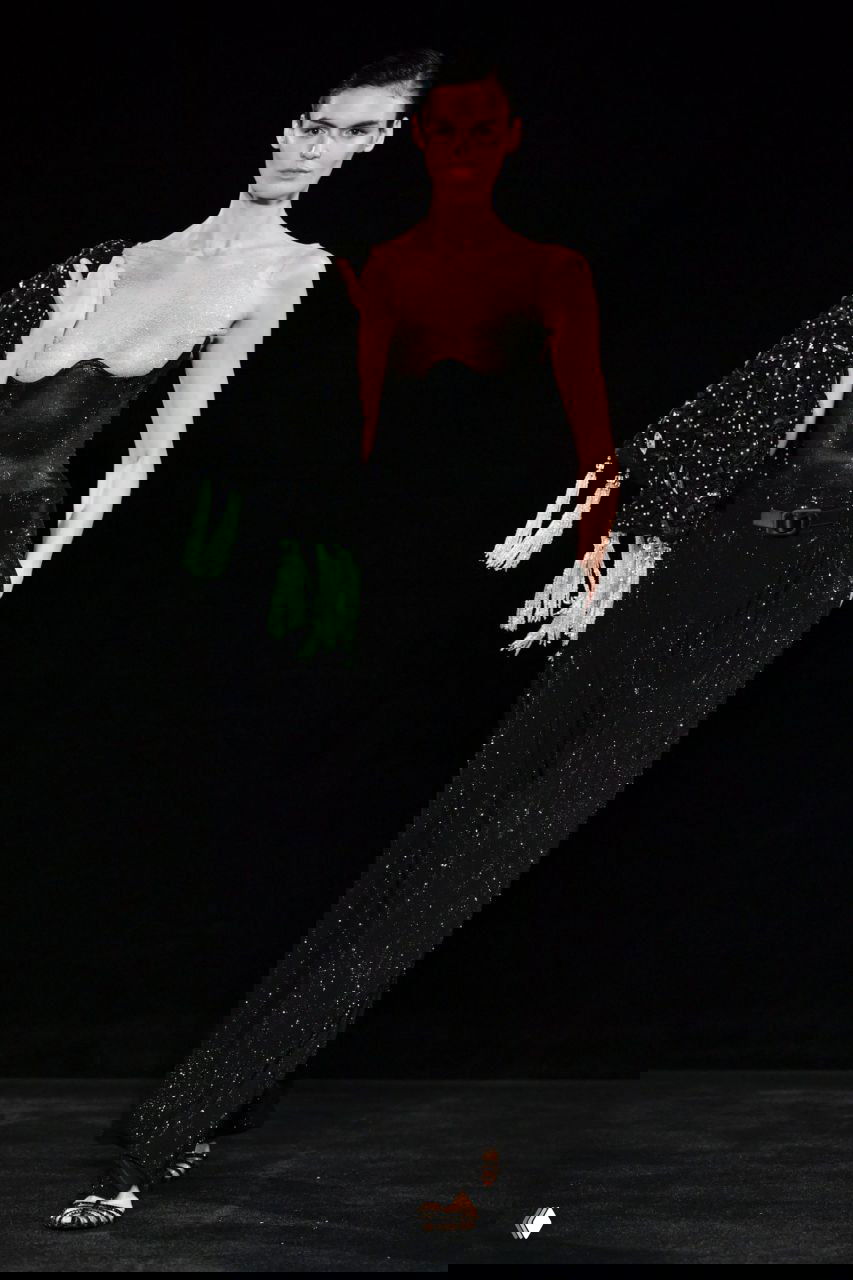 Черное платье кутюр с блеском и эффектом прозрачности в зоне декольте на подиуме Giorgio Armani, строгая поза модели и минимальный фон сцены.