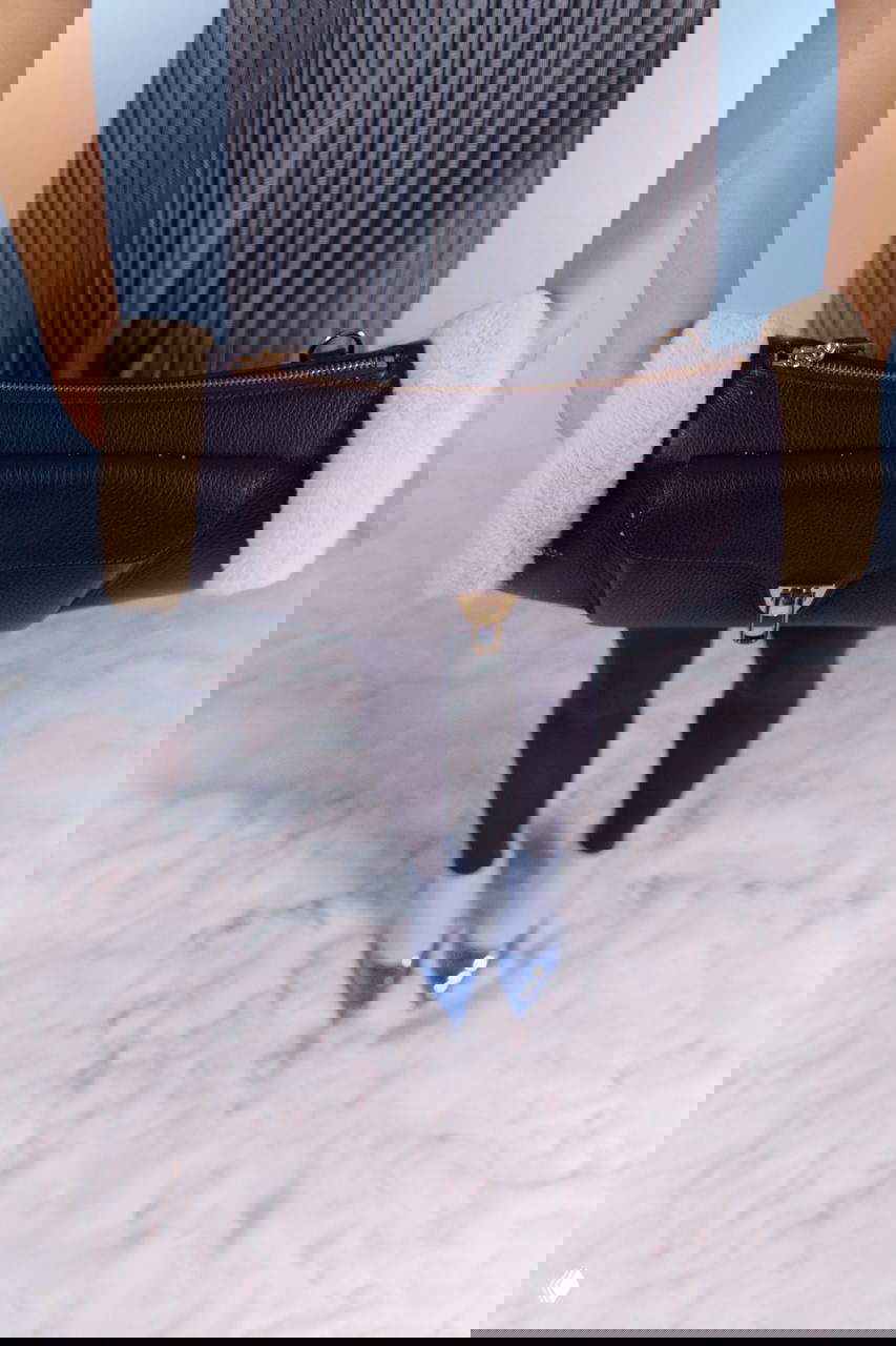 Крупный план сумки в руках модели на фоне плиссированной юбки и лаковой обуви — аксессуарный кадр из зимней студийной съёмки в редакции.