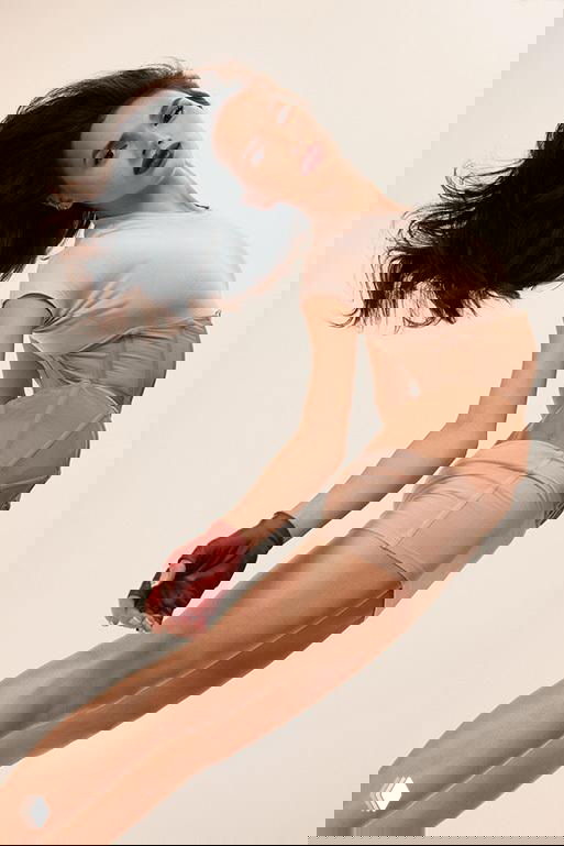 Алина Загитова в динамичной студийной позе для Marie Claire: прыжок/переход, бежевый костюм, акцент на линии тела и спортивной грации.