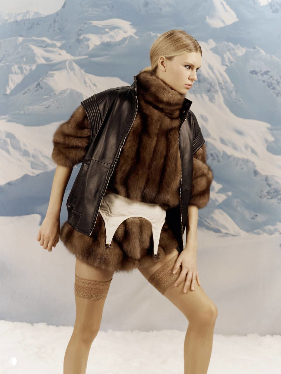 Модель в объёмной белой меховой парке и высоких ботинках на фоне горного задника — зимняя гламурная эстетика для редакционного разворота.