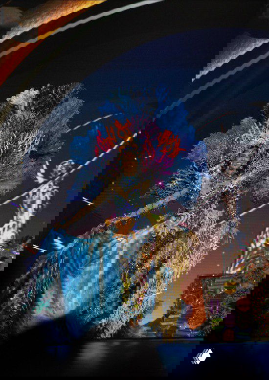 Пышный сценический костюм с яркими синими и оранжевыми элементами, сложным головным убором и морскими мотивами, показ на сцене.