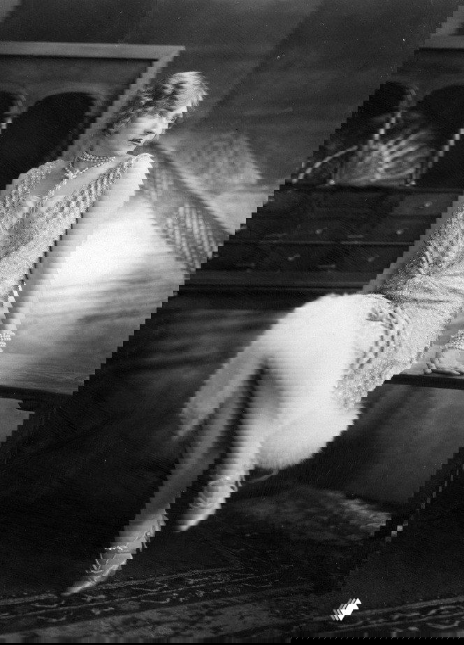 Чёрно‑белое портретное фото в стиле 1930-х: женщина в элегантном платье с пушистой меховой опушкой по низу, жемчужные украшения и интерьер джазовой эпохи.