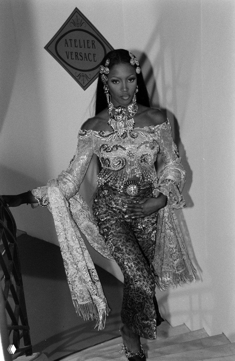 Чёрно-белое фото модели в роскошном украшенном костюме на подиуме — выразительный образ высокой моды и театральный антураж показа.