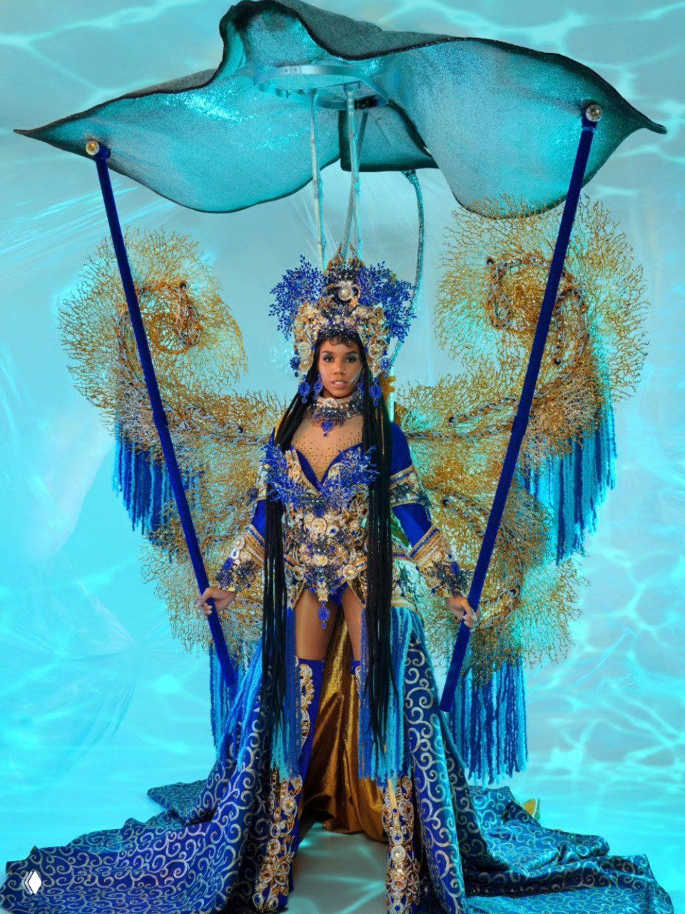 Участница в морском национальном костюме: синие ткани, декоративные кораллы и парасоль‑подобная конструкция над головой, фотосессия в студии.