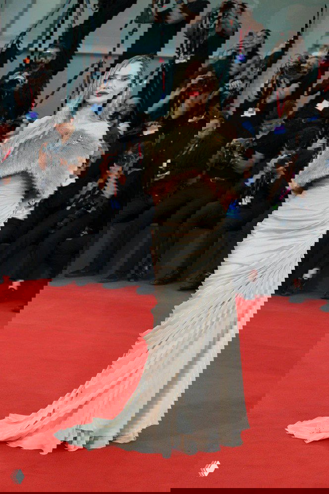 Анджелина Джоли на красной дорожке: светлое длинное платье в ретро‑стиле с меховой накидкой на плечах, папарацци на фоне.