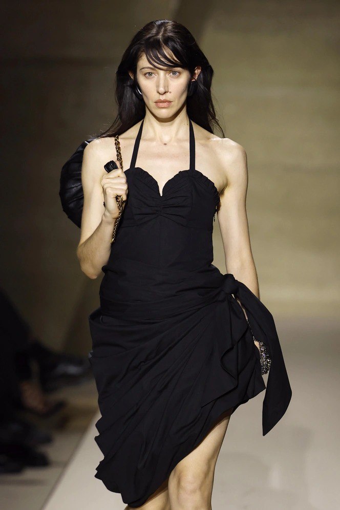 Модель в лаконичном тёмном платье с естественным макияжем и нейтральной помадой в тон кожи; образ подчёркивает натуральность и сдержанную элегантность