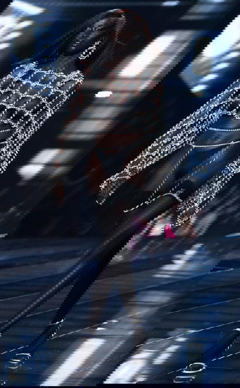 Модель в черном нижнем белье и крупной сетке из кристаллов идет по глянцевому подиуму во время вечернего шоу.