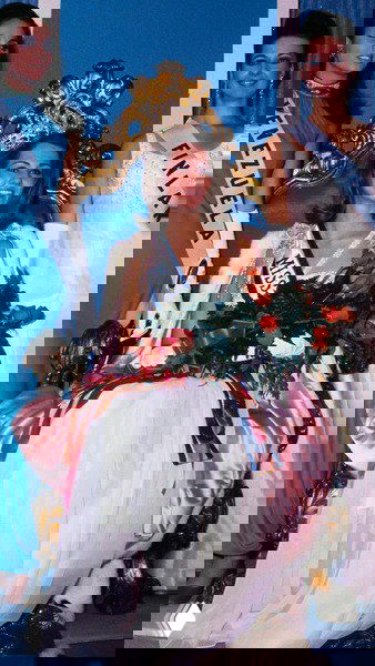 Победительница на тронике с букетом и лентой Miss Universe — портрет в платье, отражающий стандарты красоты и сценический стиль прошлых десятилетий.