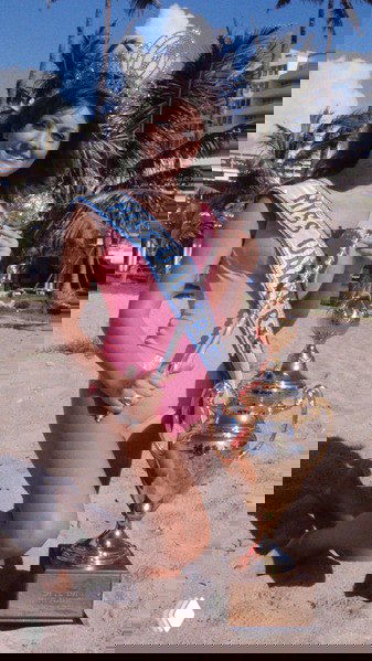 Победительница в купальнике на пляже с большим трофеем — ретро-кадр, иллюстрирующий образ конкурсанток и визуальные стандарты своей эпохи.