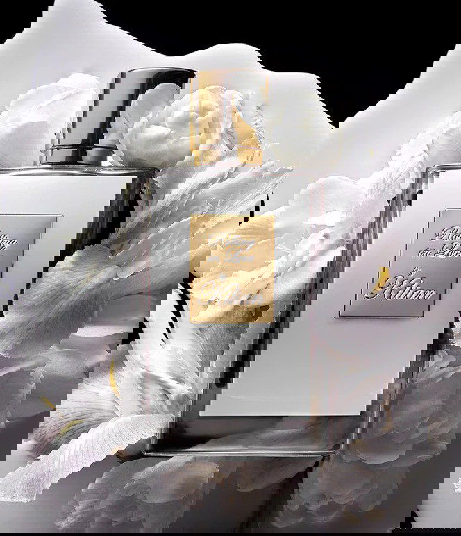 Флакон Rolling in Love от Kilian на фоне белых цветов (ирис, фрезия) — крупный рекламный план, подчёркивающий ноты ванили и бобов тонка.