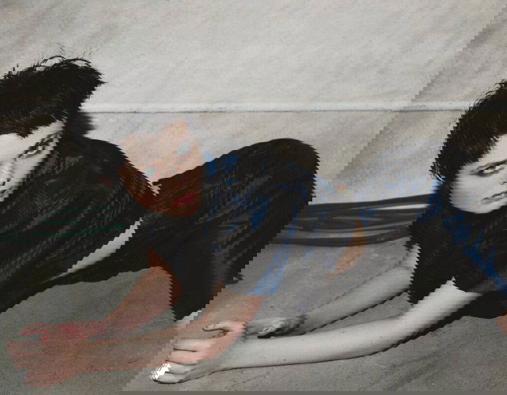 Женщина с короткой тёмной стрижкой лежит на полу в тёмном атласном наряде — крупный кадр из глянцевой модной фотосессии с выразительным макияжем.