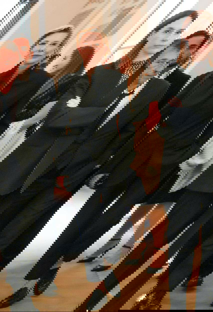 Кейт Бланшетт в чёрном строгом костюме идёт по коридору Ватикана в окружении делегатов и охраны на официальной встрече.