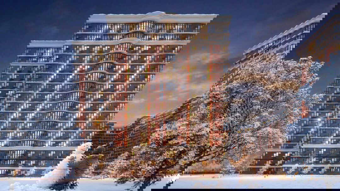 Заснеженный двор на фоне фасада жилого комплекса «Самолет» в Краснодаре; человек лепит снеговика у высоких панорамных окон и теплых огней в окнах.