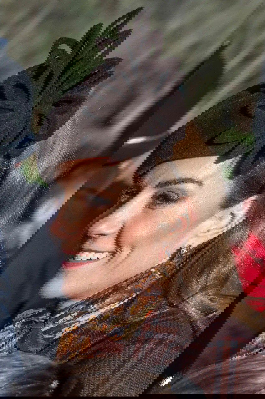 Крупный план женщины в тёмной фетровой шляпке с декоративным элементом и лёгким макияжем на рождественском событии.