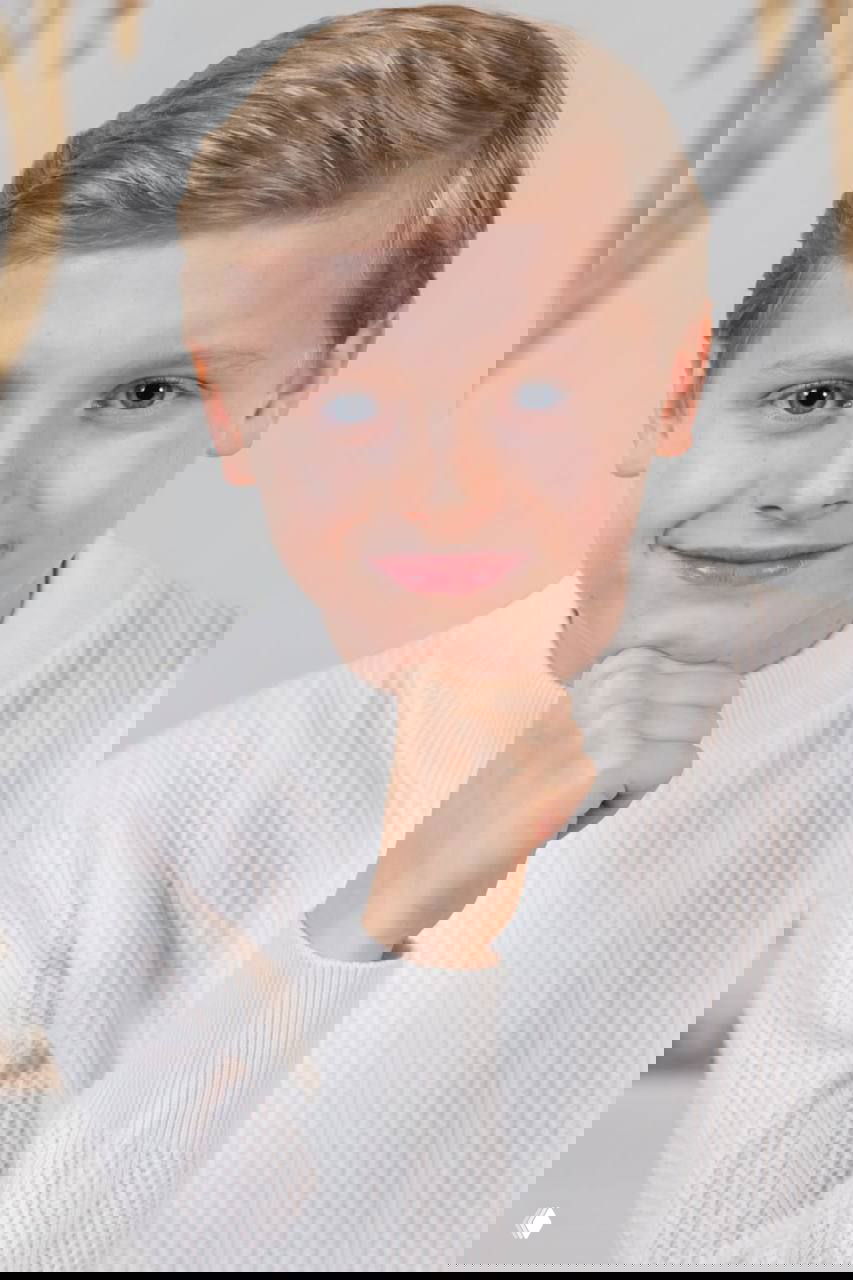 Официальный портрет принца Монако Жака, 11 лет: портрет крупным планом в белом свитере, лёгкая улыбка и нейтральный интерьер официальной фотосессии.