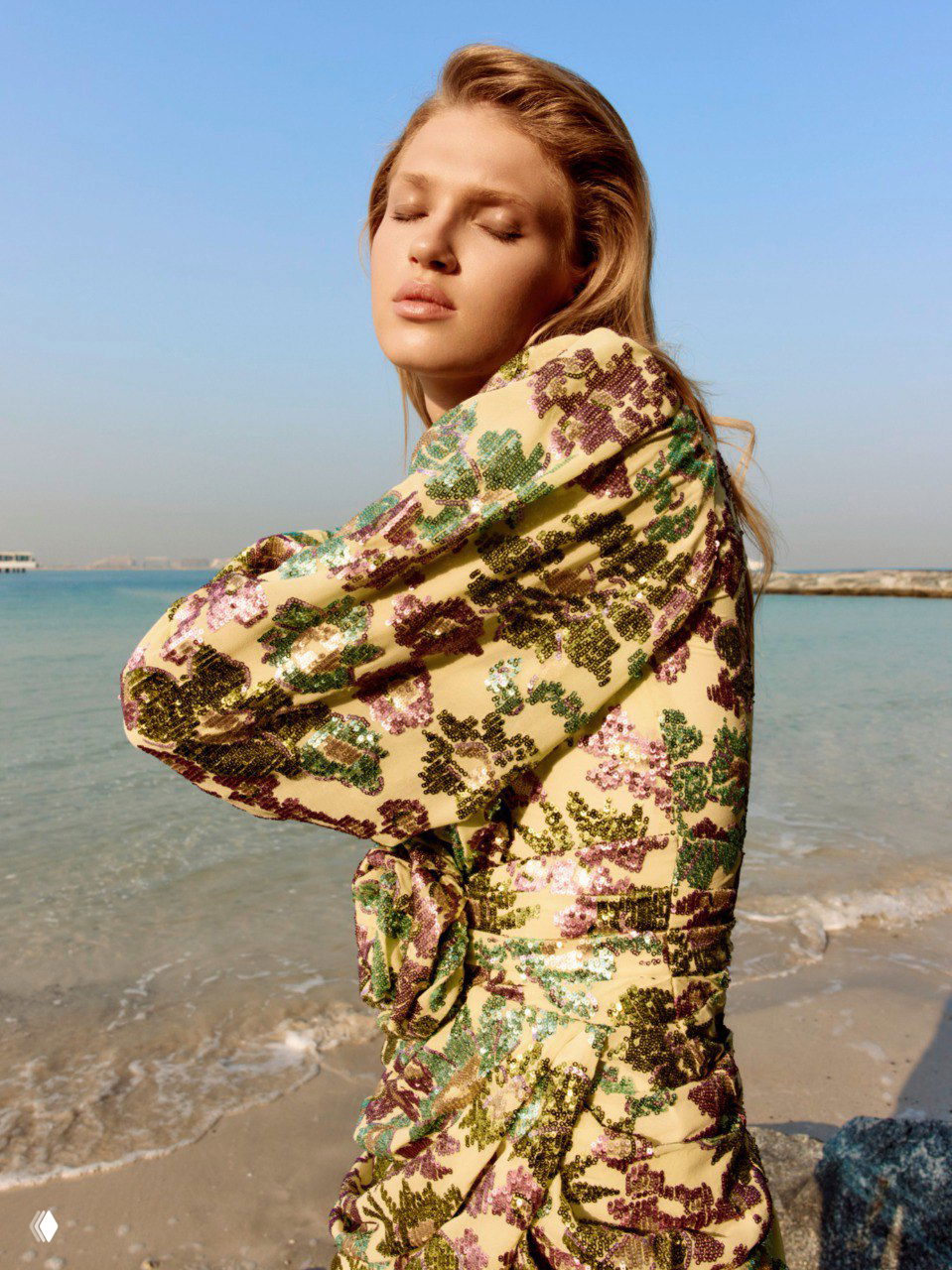 Фэшн-кадр модели в блестящем цветочном платье на фоне моря — сочетание пайеток и природного света подчёркивает праздничность образа.