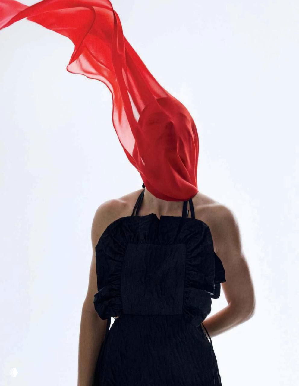 Артистичный кадр: полупрозрачный красный шарф закрывает лицо модели, плавные складки ткани на контрастном светлом фоне.