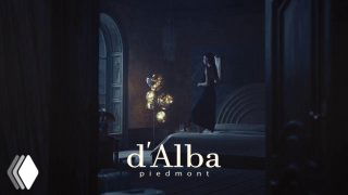 Тёмный атмосферный кадр кампейна d'Alba с логотипом бренда внизу кадра; художественная сценография и модель в глубине композиции.