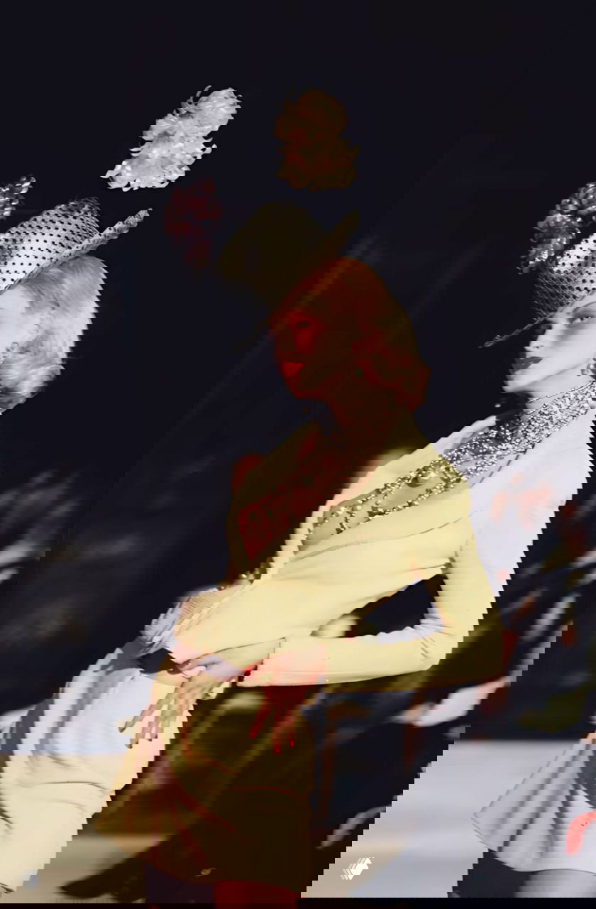 Модель в бледно‑желтом костюме и высоком шляпном украшении на показе Dior осень‑зима 1997, сложная шляпная конструкция и винтажные украшения.