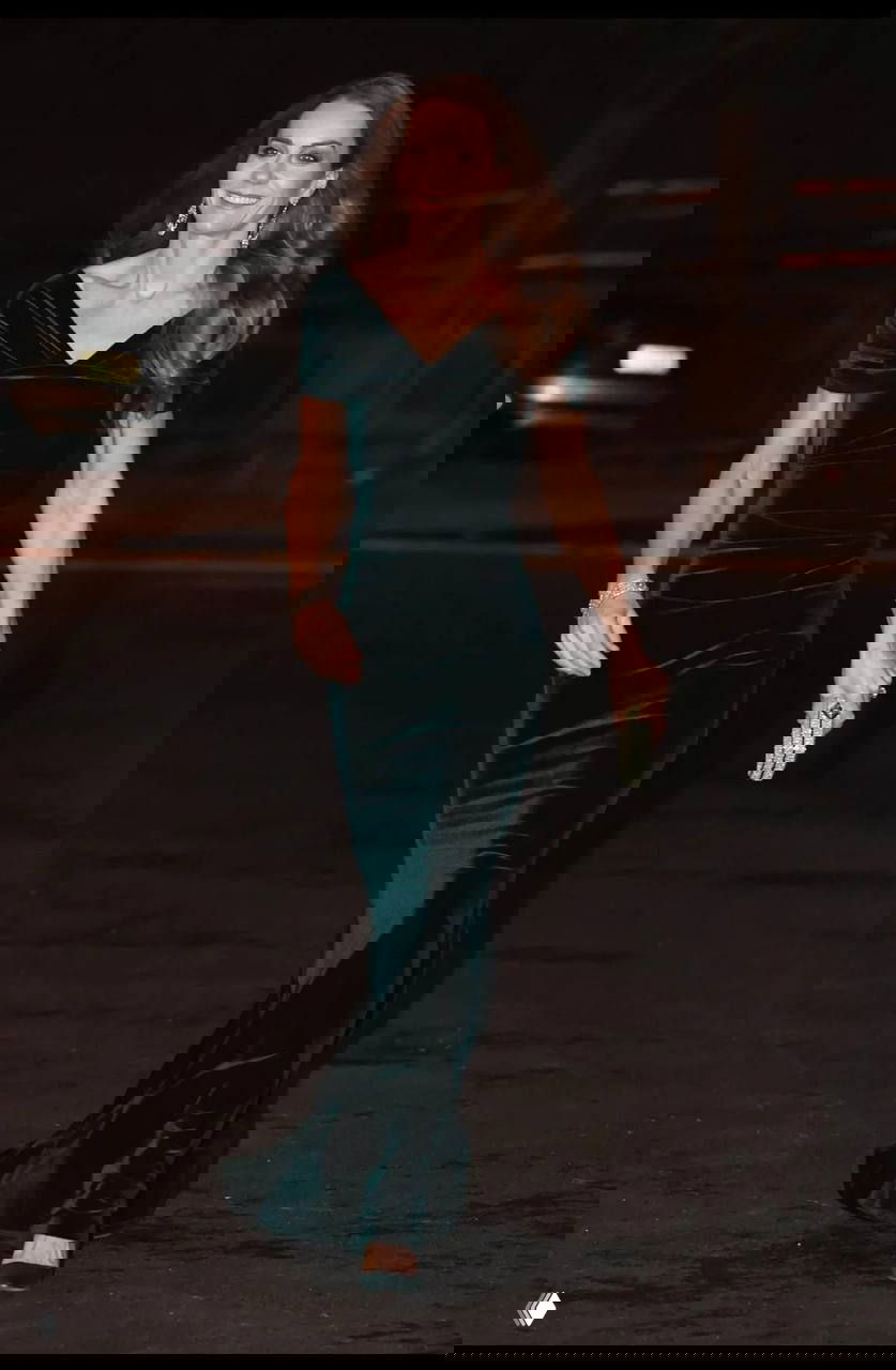 Крупный план женщины в длинном тёмно‑зелёном платье, она идёт по красной дорожке на вечернем мероприятии.