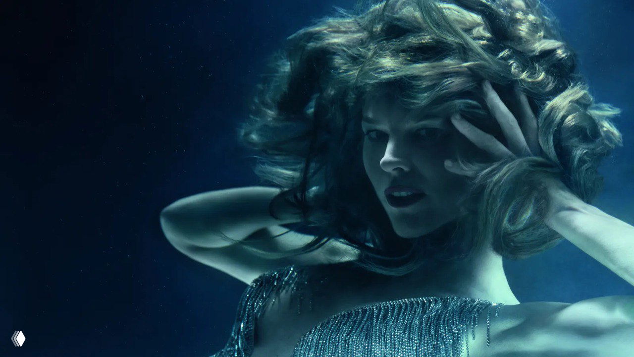 Подводный образ: модель в глубоком синем оттенке, волосы развеваются словно вода, фотография передаёт эстетику стихии воды и плавности движения.